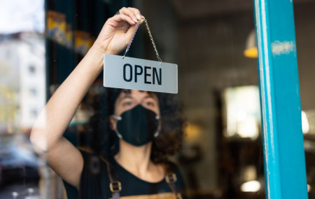 Frau mit Mundschutz hängt Geöffnet Schild in Geschäftstür auf