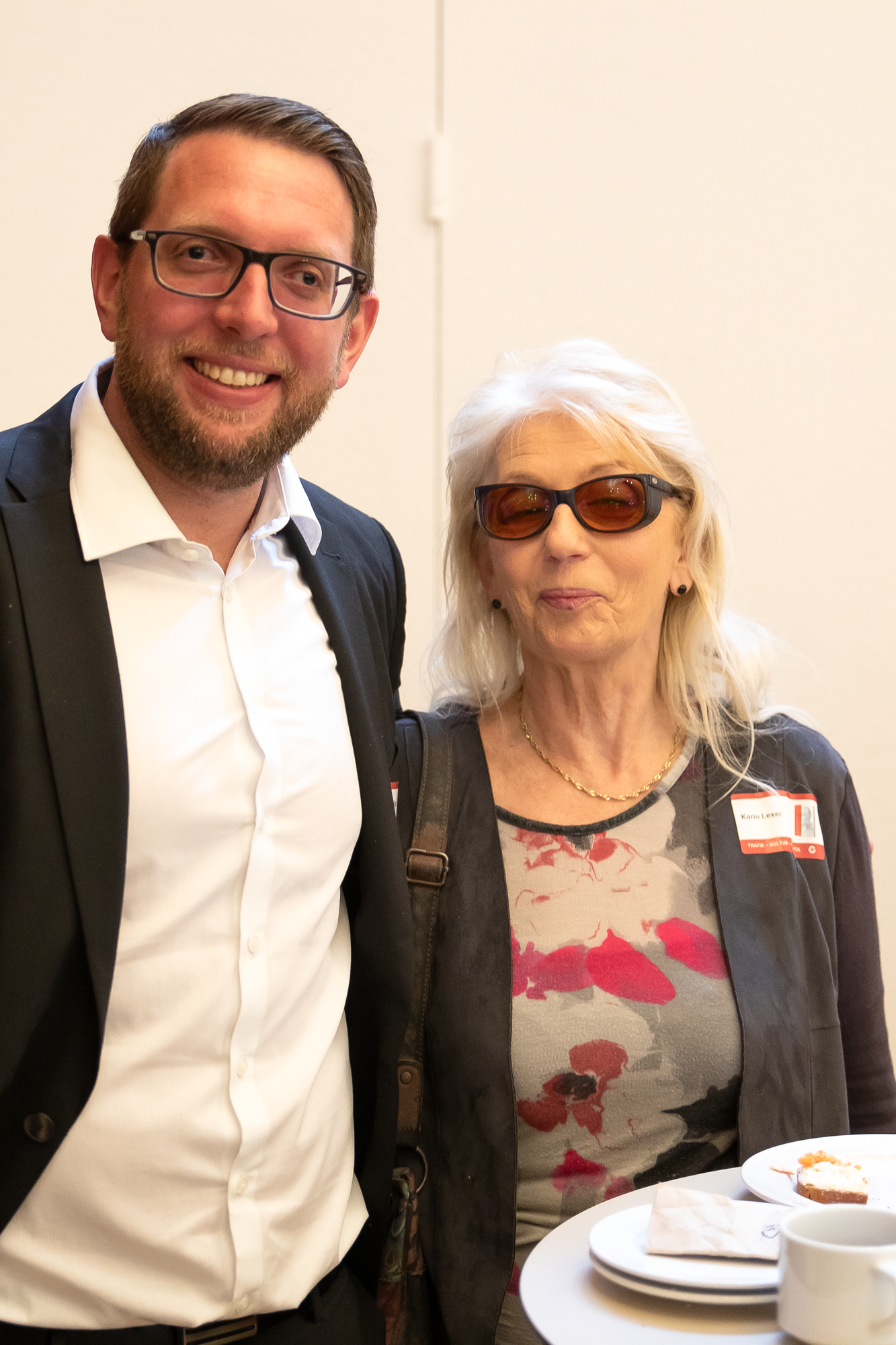 Ein Mann in einem weißen Hemd und eine Frau in  einem bunten Oberteil schauen in die Kamera