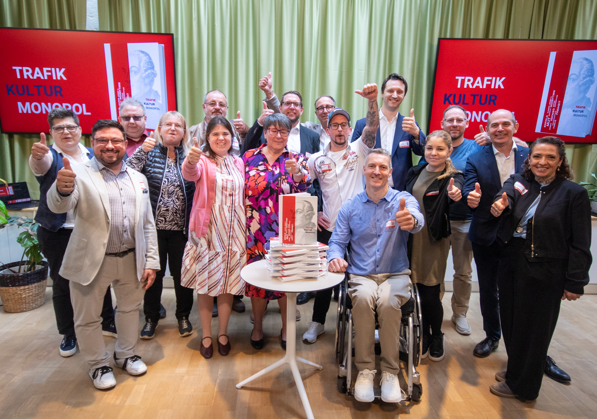 Ein Ein Gruppenfoto der Trafikanten und Trafikantinnen, die im Trafikbuch beschrieben werden, die einen Daumen nach oben zeigen