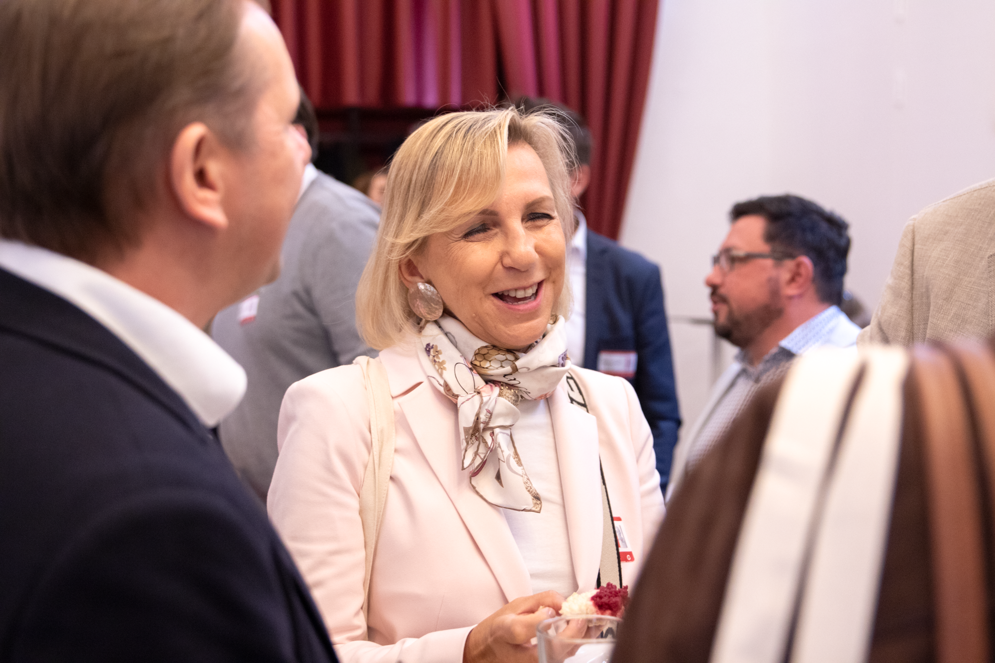 Im Vordergrund befindet sich eine Frau mit blonden Harren und hellrosa Oberteil