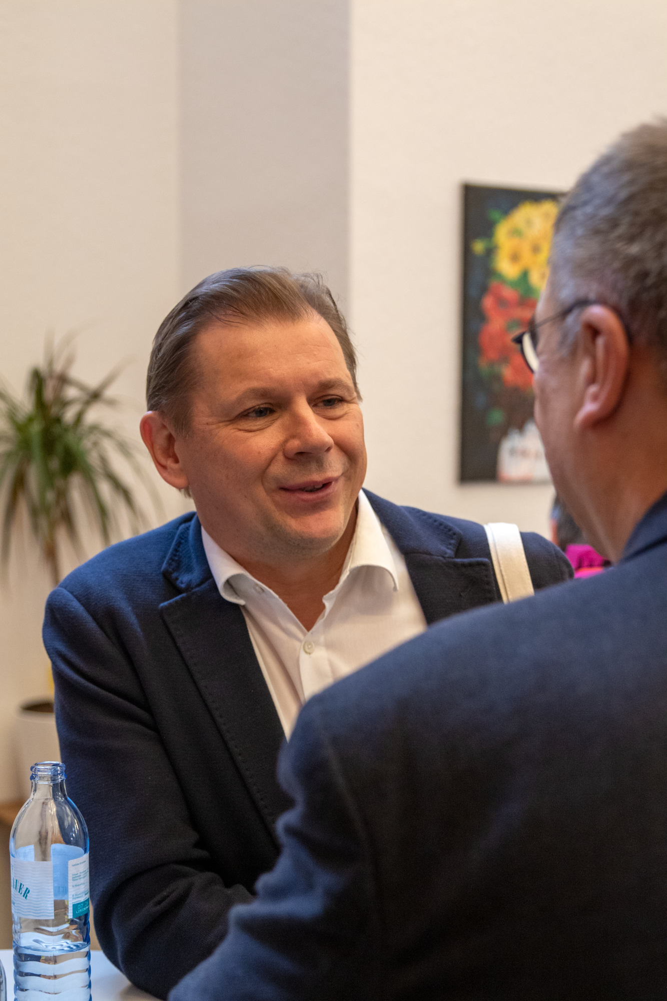 Ein Mann in einem blauen Sakko und einen weißen Hemd unterhalt sich mit einem Mann in einen blauen Sakko