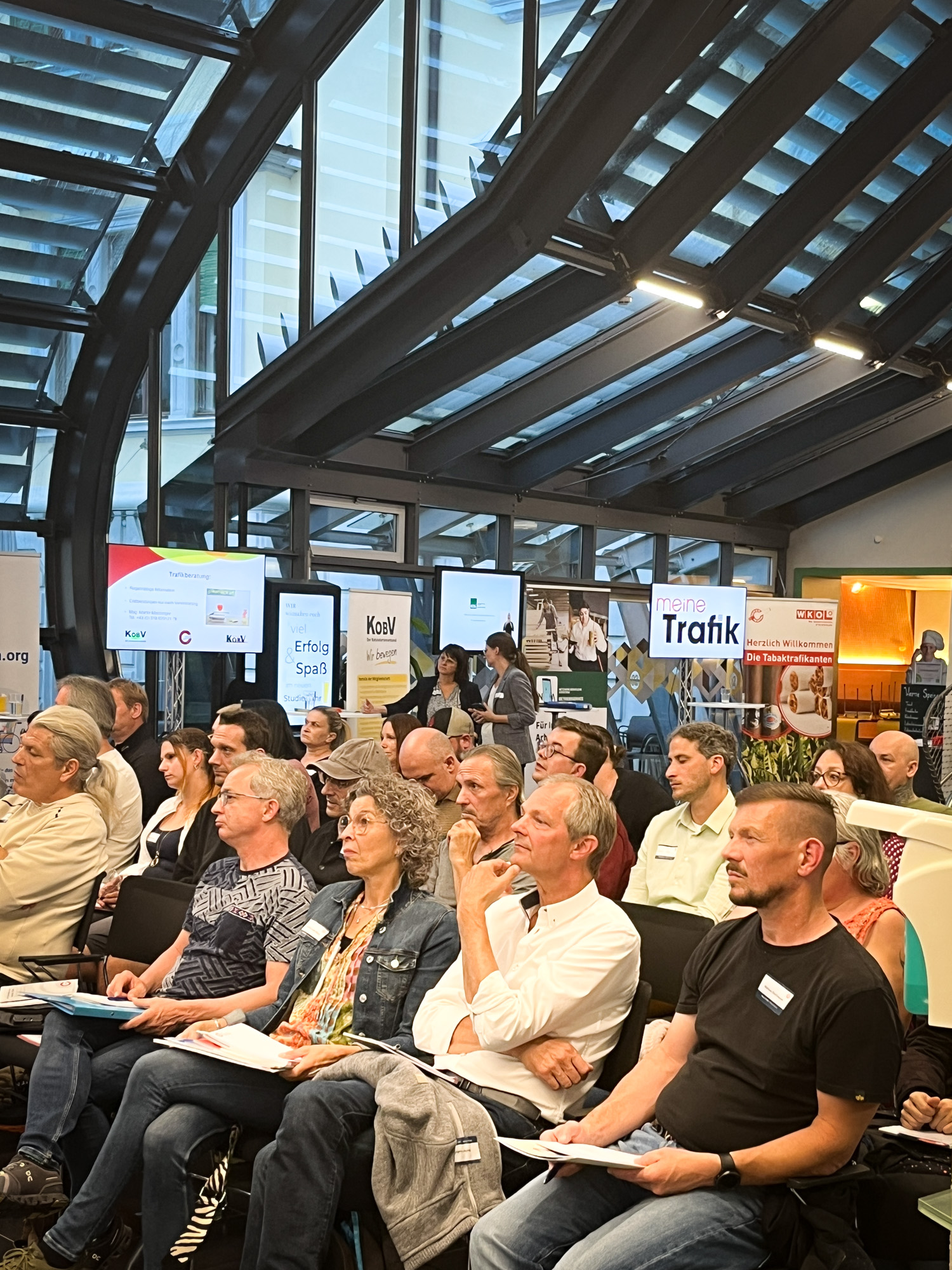 Ein Foto vom Publikum. Mehrere Personen sind in Reihen aufgegliedert und lauschen einen Vortrag. 