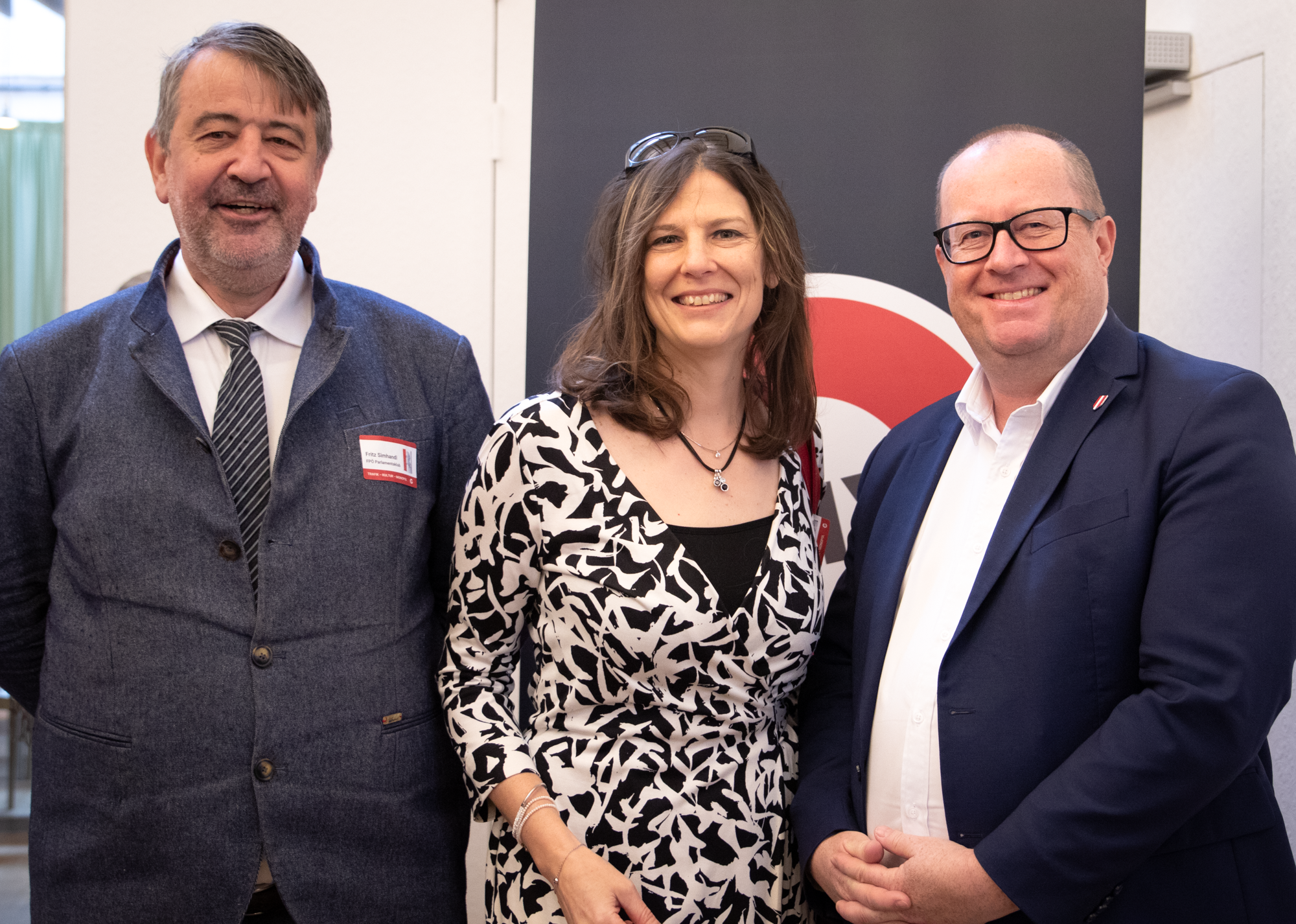 Drei Personen, eine Frau zwischen zwei Männern lächeln in die Kamera