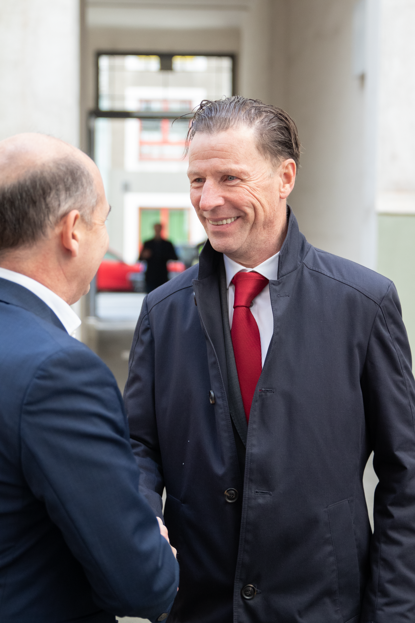 MVG Geschäftsführer begrüßt einem Mann mit einer roten Krawatte und einer blauen Jacke