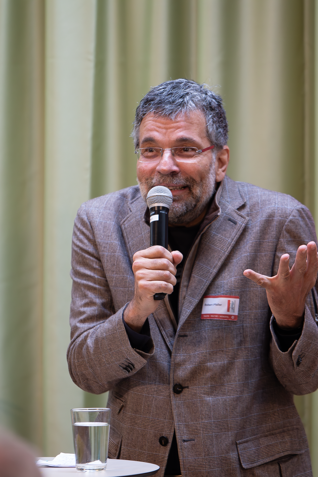 Ein älterer Herr steht auf der Bühne und präsentiert in einem braun, grauen Sakko das Trafikbuch