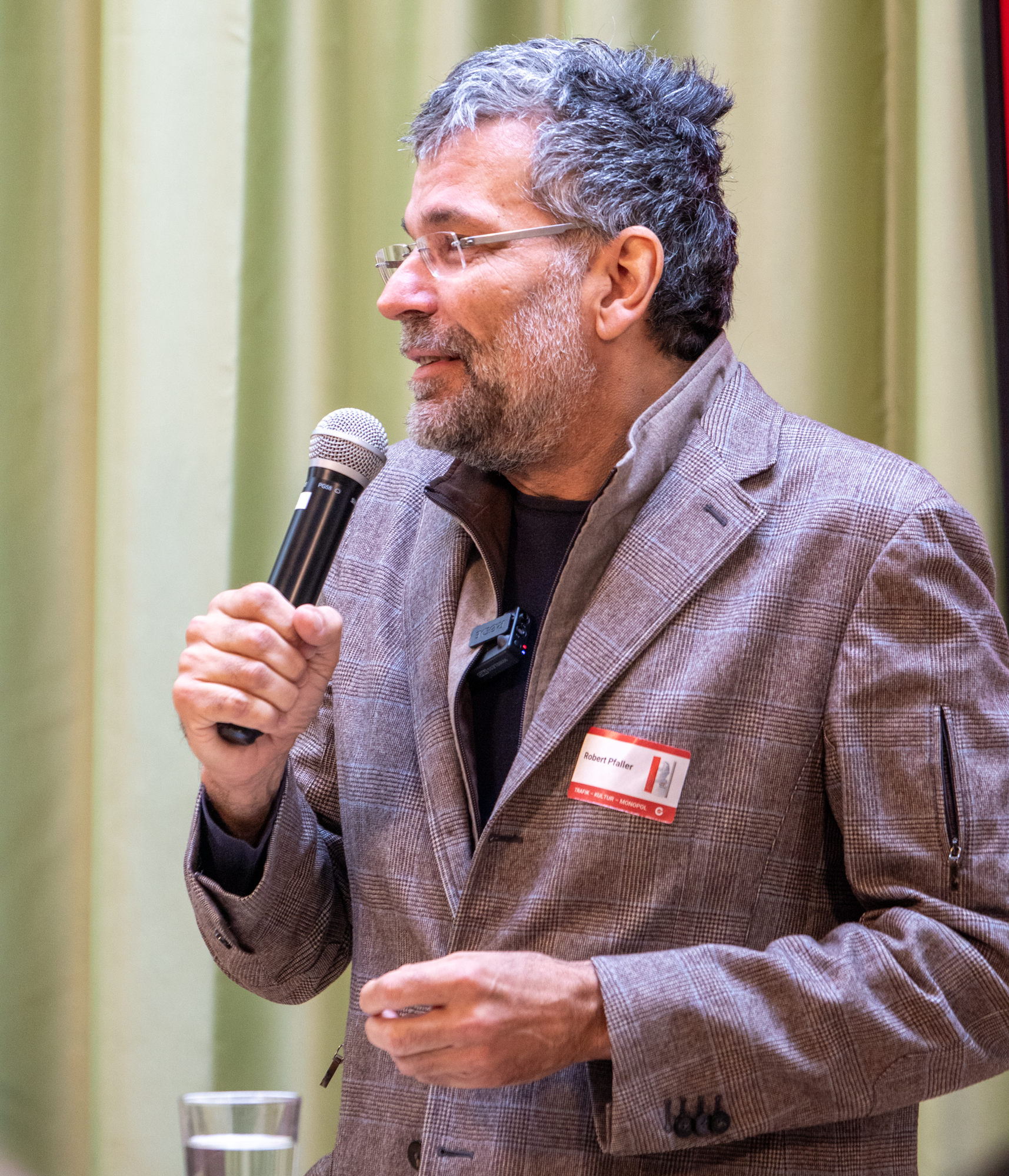 Ein älterer Herr steht auf der Bühne und präsentiert in einem braun, grauen Sakko das Trafikbuch