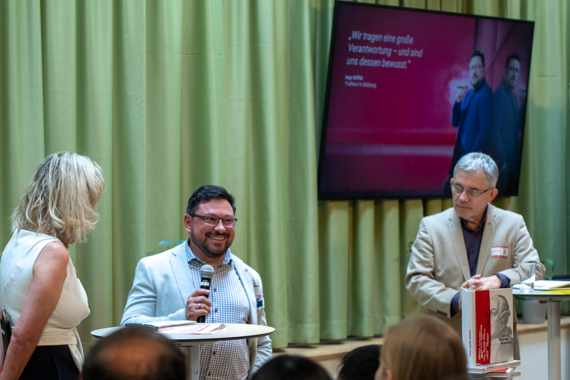 Monopolstellenleiterin und Monopolstellenleiter stehen mit Trafikant auf der Bühne