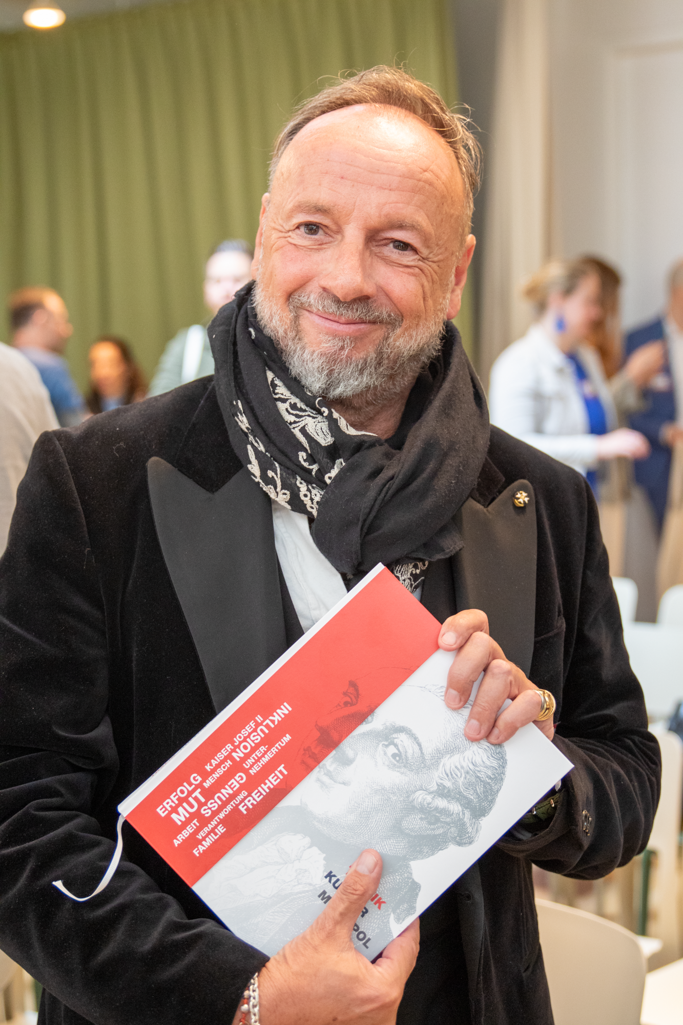 Ein Mann mit einer schwarzen Jacke hält ein Exemplar vom Trafikbuch in dei Kamera