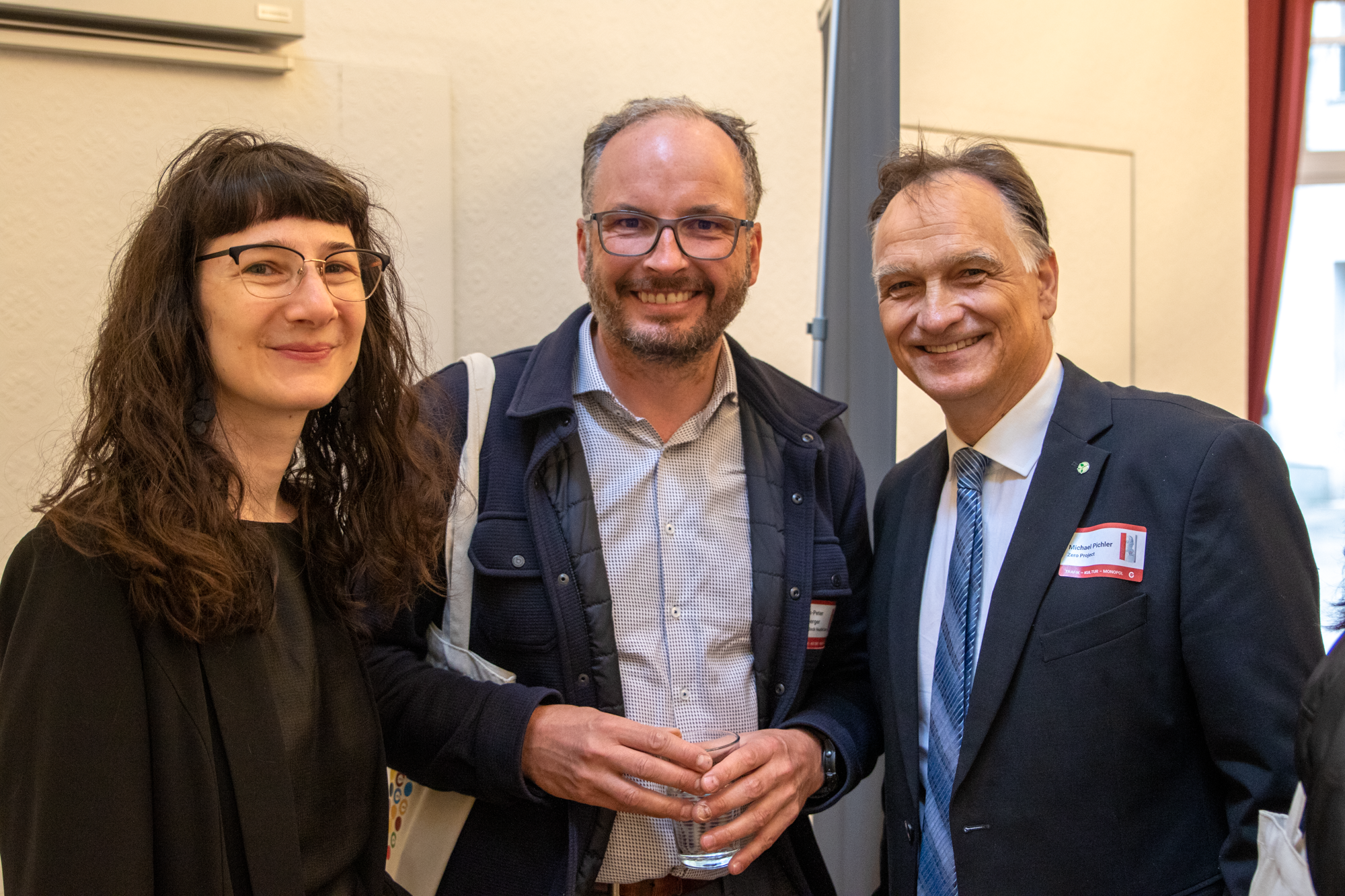 Eine Frau steht neben zwei Herren, alle lächeln in die Kamera