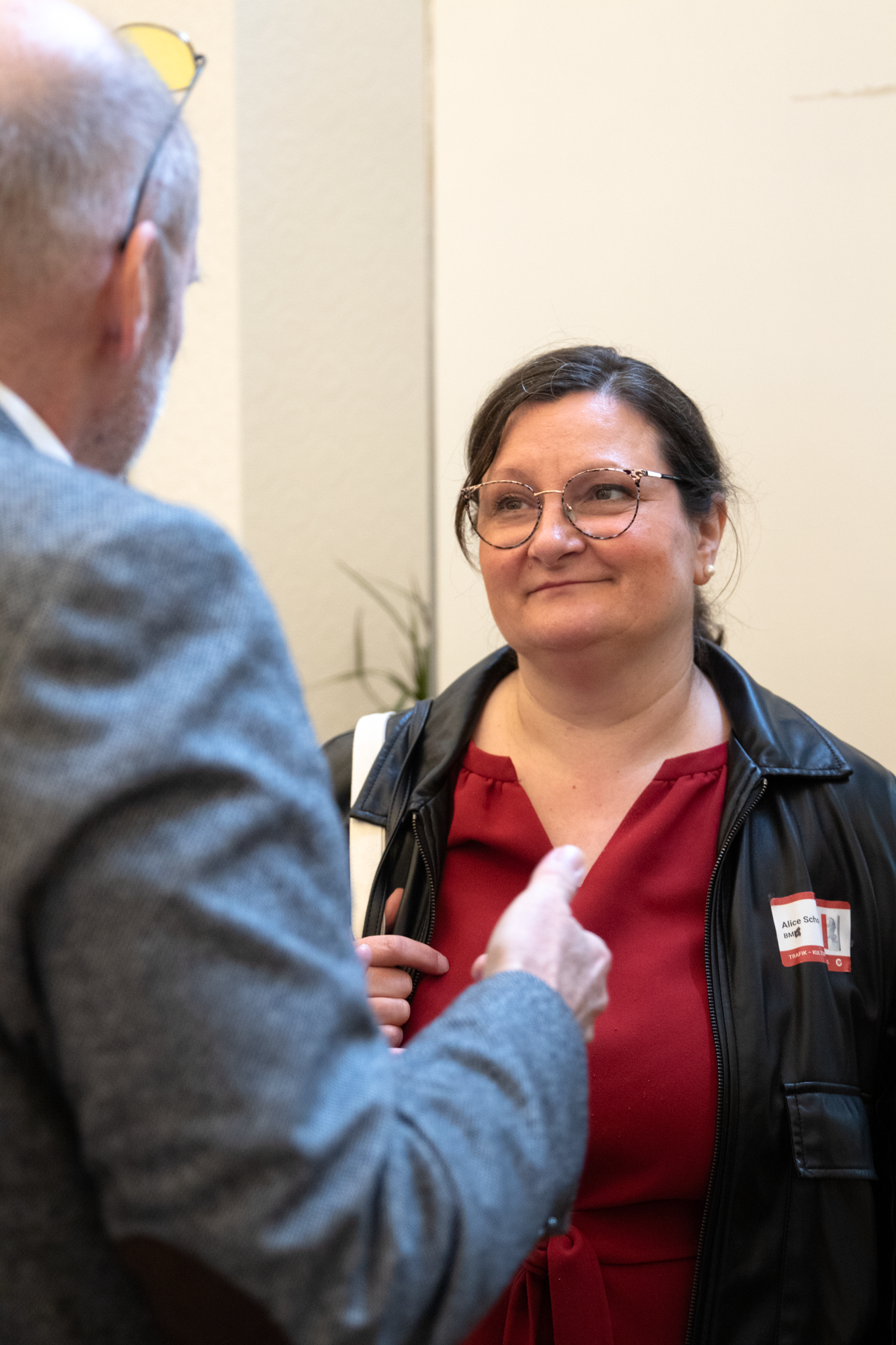 Eine Besucherin in einem roten Oberteil und einer schwarzen Lederjacke unterhaltet sich mit einem Monopolstellenleiter