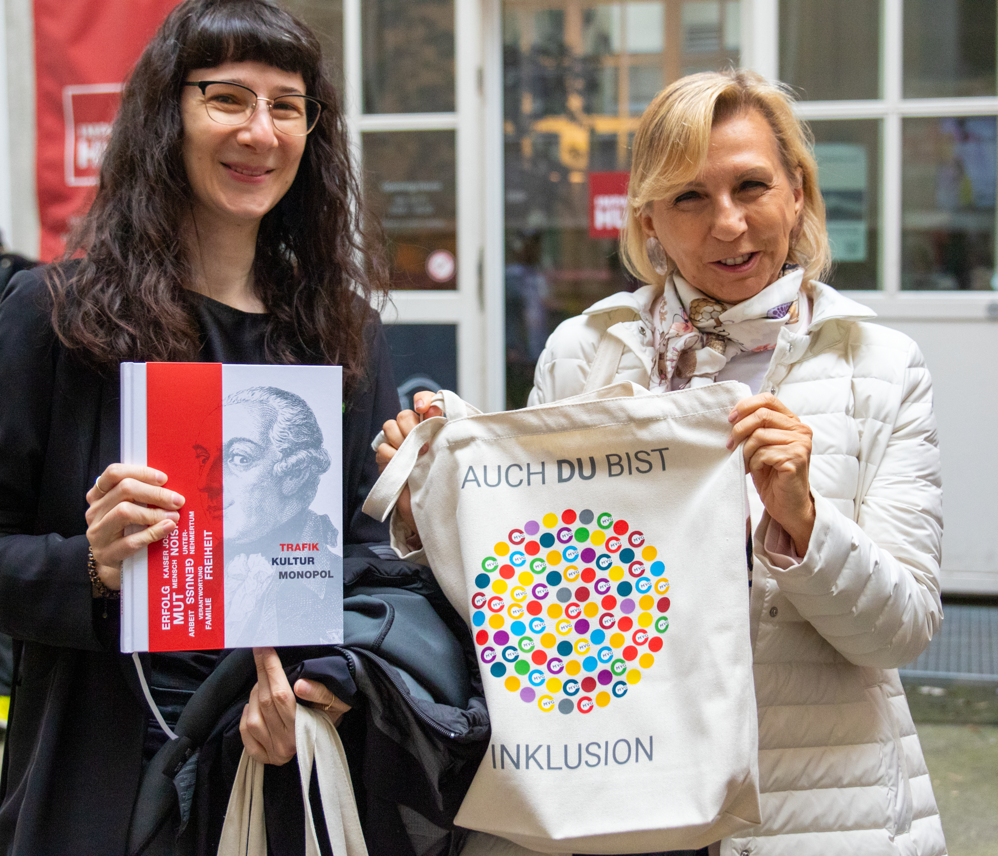 Zero Projekt Mitarbeiterinnen präsentieren Trafikbuch und MVG Jutebeutel mit der Aufschrift "auch du bist Inklusion"