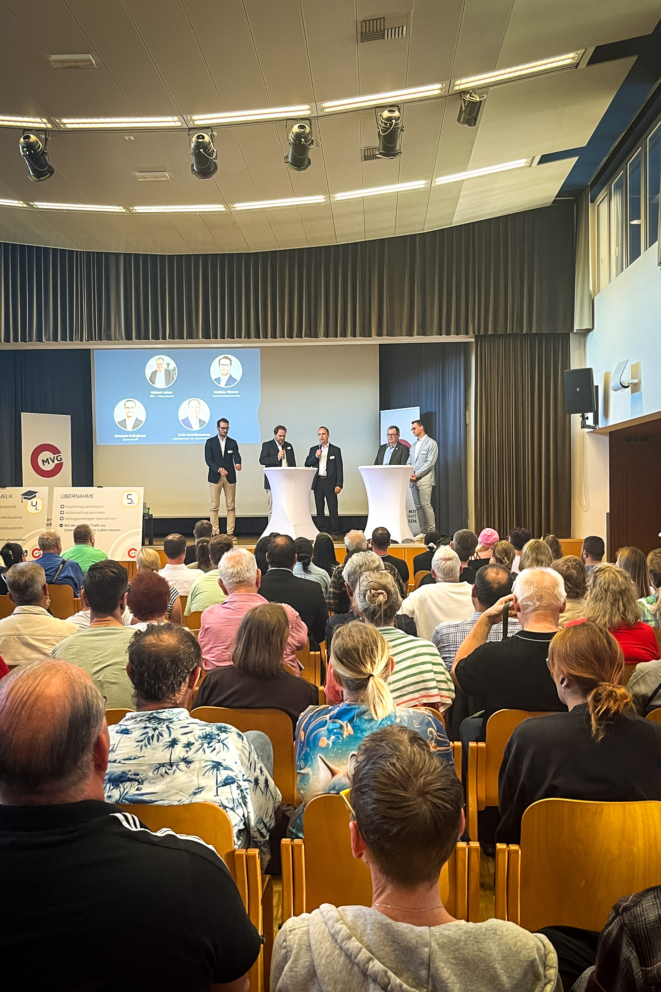 Blick aus dem Publikum. Die Interessenten und Interessentinnen sitzen in Reihen und blicken auf die Bühne, wo mehrere Personen personen sich und Ihre Organisation vorstellen. 