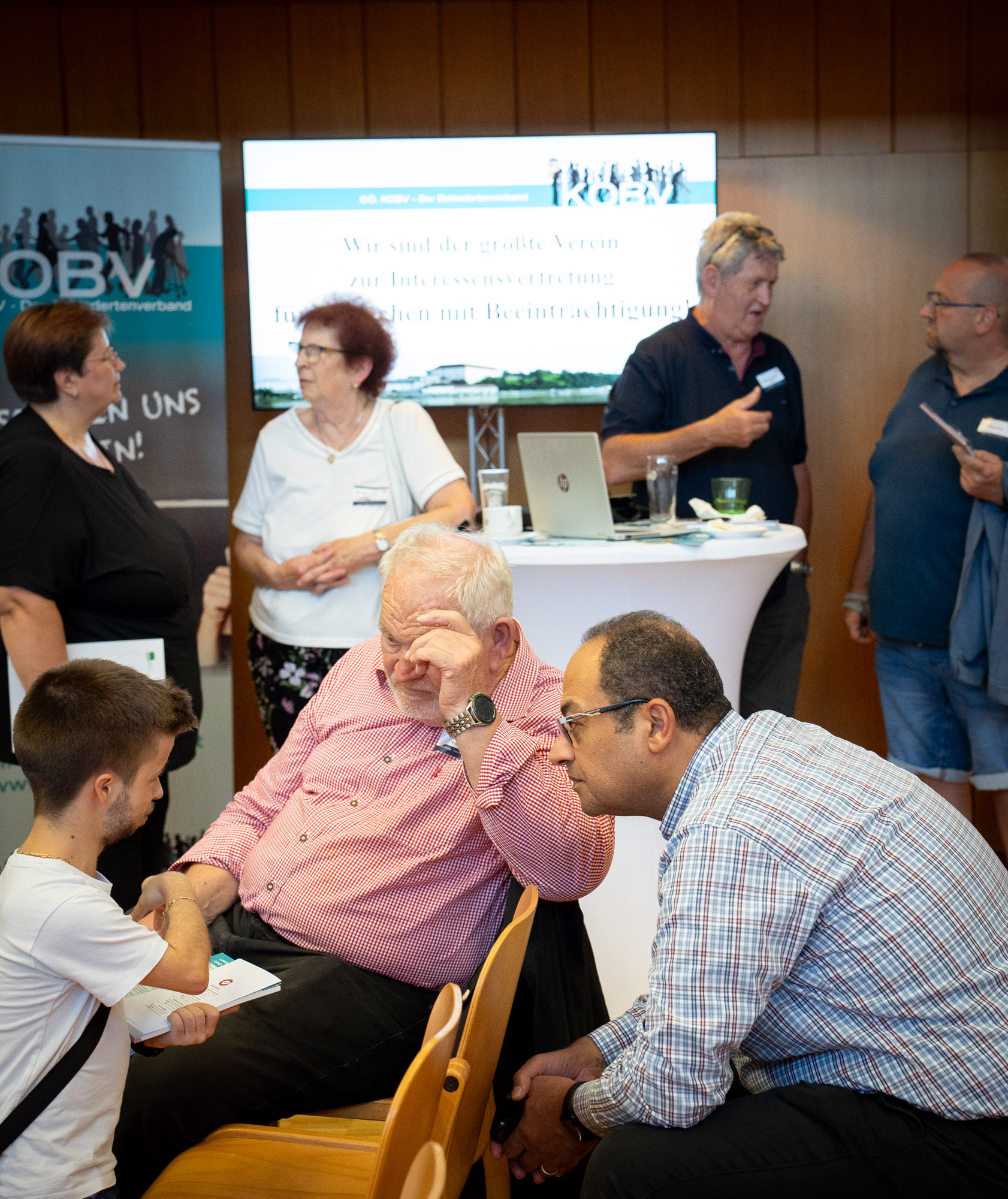 Auf dem Bild sind im Vordergrund drei Interessenten, die sich über die Veranstaltung unterhalten, im Hintergrund befindet  sich ein KOBV Stand mit Mitarbeitern und zwei weiteren Interessenten.
