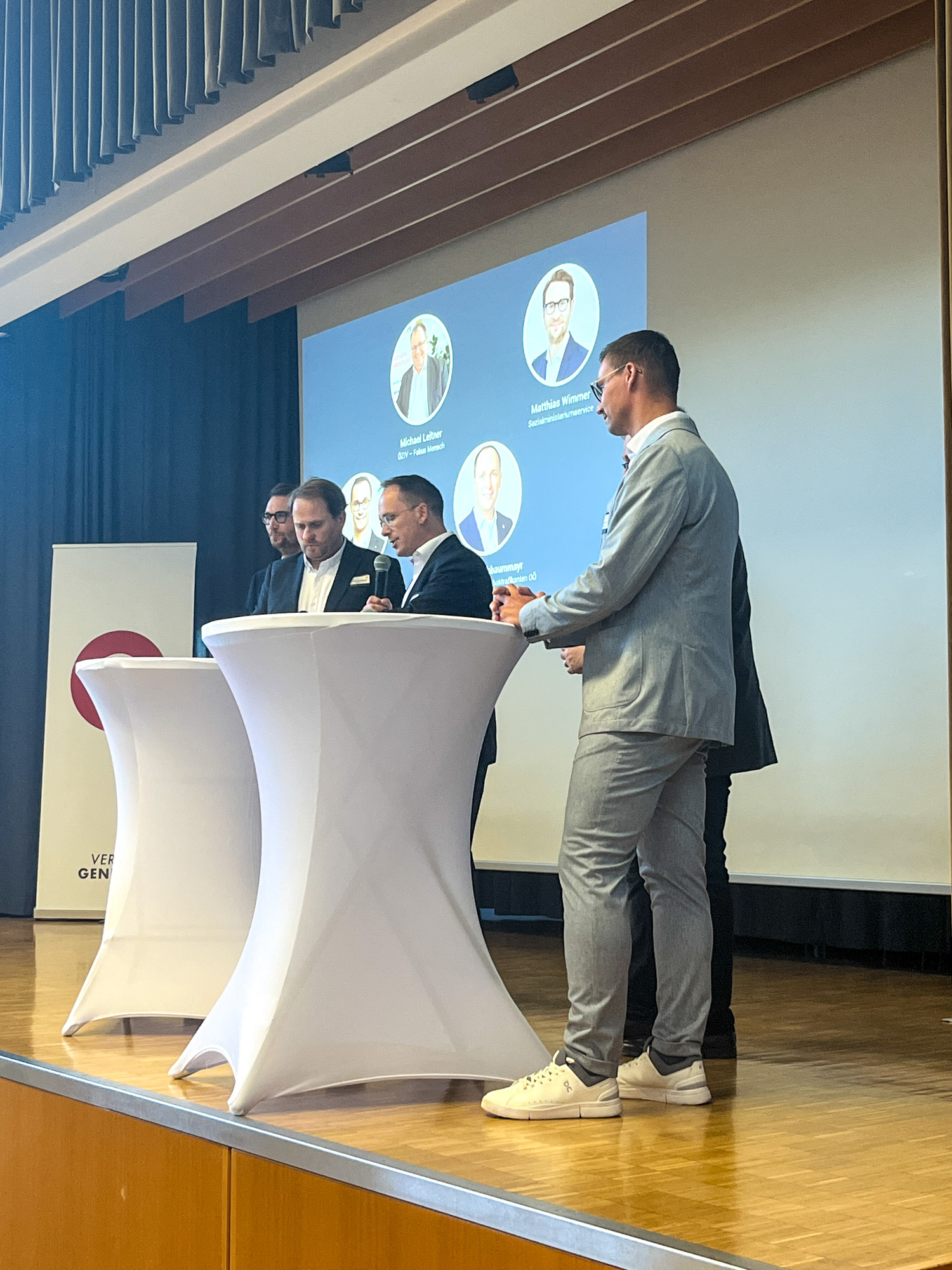 Blick auf die Bühne, wo fünf männliche Organisationspartner sich und ihre Organisation vorstellen. 