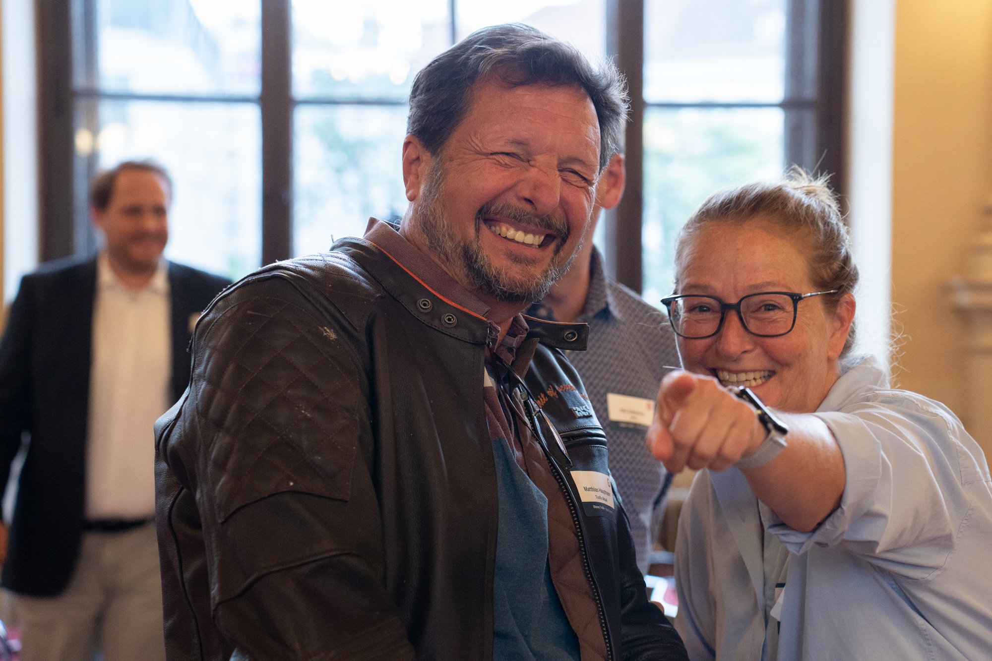 Zwei Menschen sind im Vordergrund eines Bildes zu sehen und zeigen und lachen in die Kamera