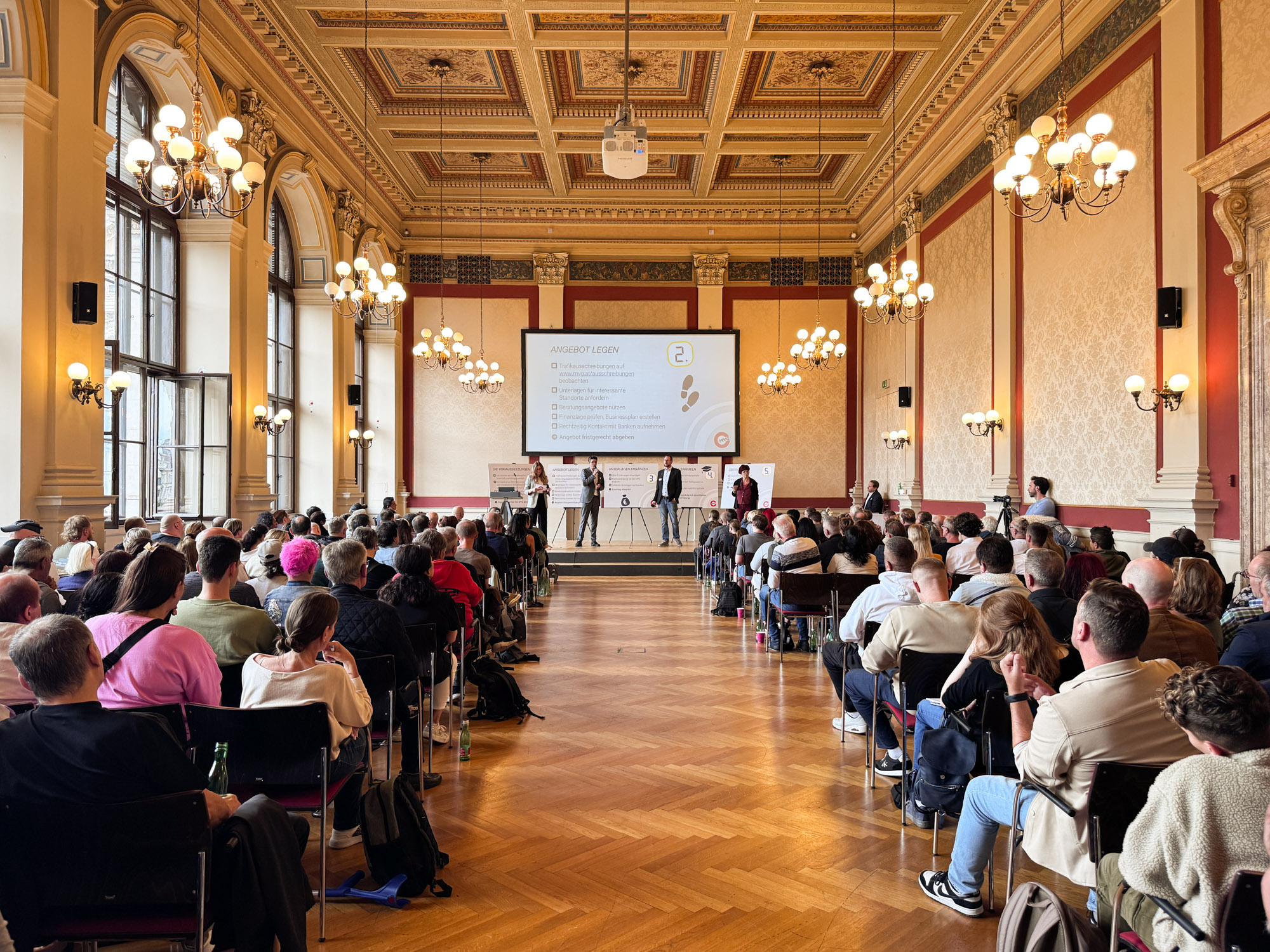 Bild von einem großen Saal mit Interessenten und Interessentinnen die einen Vortrag anhören